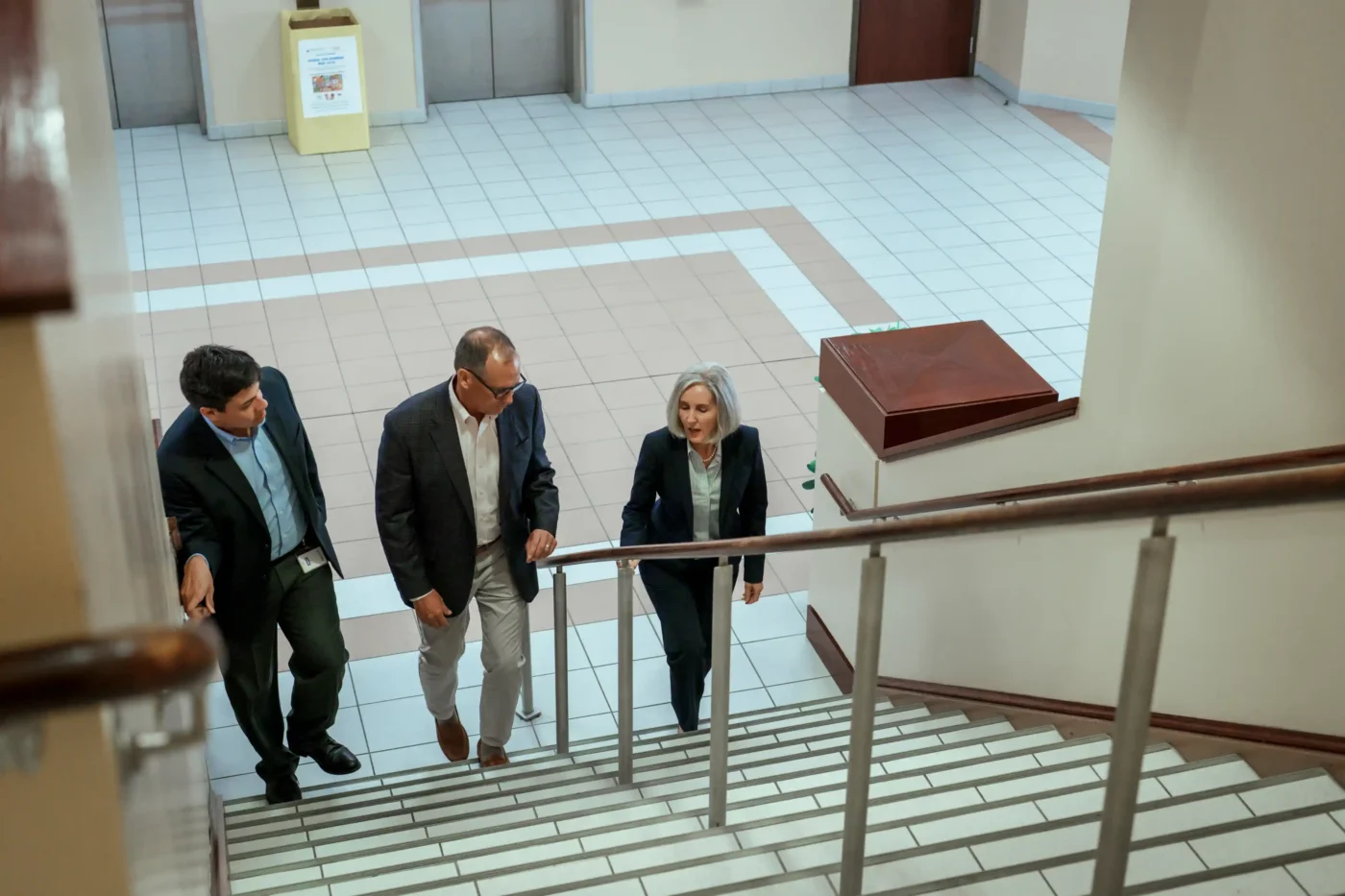 Two men and a woman are taking up stairs